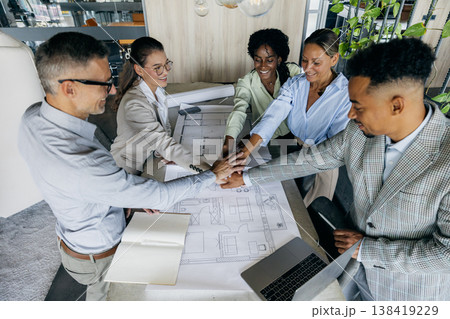 Group gathers around table displaying plans with optimistic determination Group gathers around table displaying plans with optimistic determination 138419229