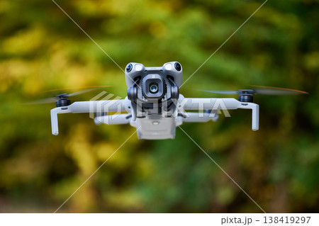 A person controls a drone outdoors, operating it skillfully among trees and greenery. The drone captures beautiful aerial footage during daylight. A person controls a drone outdoors, operating it skillfully among trees and greenery. The drone captures beautiful aerial footage during daylight. 138419297