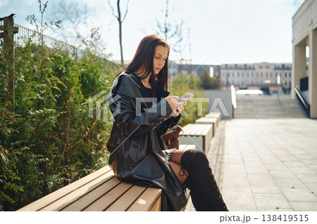 Woman using smartphone while sitting on bench in urban area on sunny day Woman using smartphone while sitting on bench in urban area on sunny day 138419515