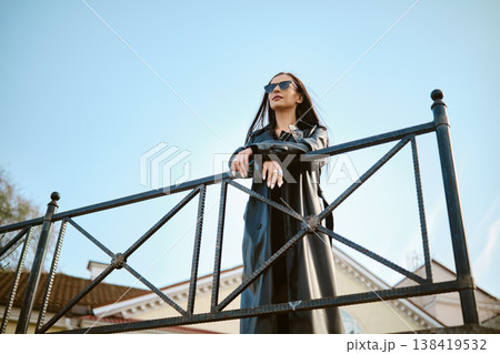 Woman in sunglasses stands on a metal railing looking at the sky during daytime 138419532