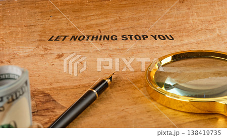 LET NOTHING STOP YOU on wood. Fountain pen, rolled cash, gold magnifier nearby LET NOTHING STOP YOU on wood. Fountain pen, rolled cash, gold magnifier nearby 138419735
