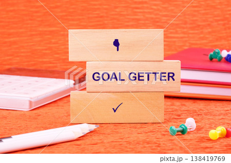 Goal Getter on blocks, surrounded by office tools on orange, signifying overcoming challenges to achieve success 138419769