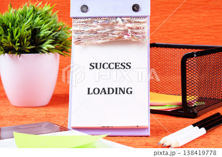 A daily calendar stands prominently on a warm orange desk, showing the motivating phrase Success Loading 138419778