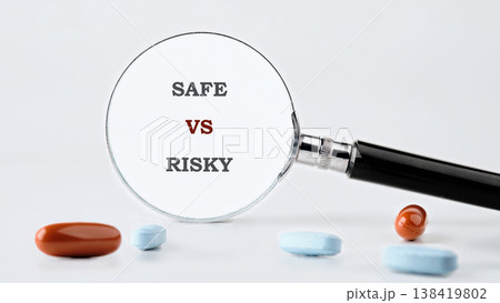 A gleaming magnifying glass centers on the words safe versus risky. Diverse capsules lay scattered, prompting a thoughtful evaluation of options A gleaming magnifying glass centers on the words safe versus risky. Diverse capsules lay scattered, prompting a thoughtful evaluation of options 138419802