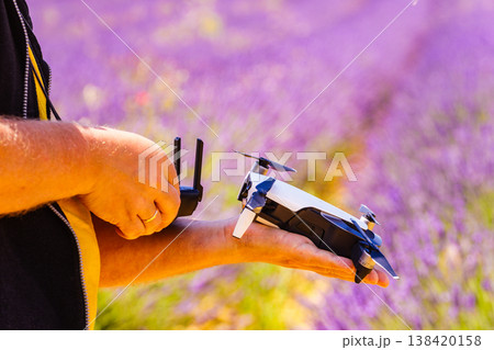 Person holds a drone in hand and remote control in the other hand while standing in a field of levender flowers Person holds a drone in hand and remote control in the other hand while standing in a field of levender flowers 138420158