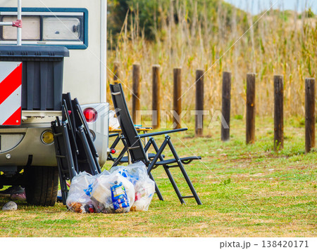 Camper vehicle camping on nature with camp chairs outside and many trash bags 138420171