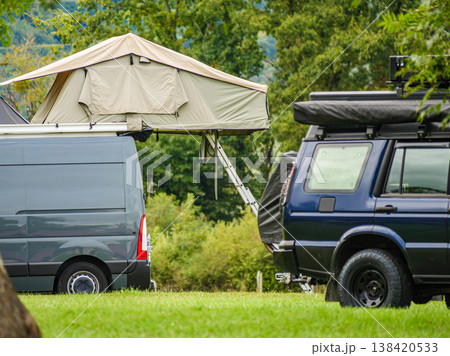 Camping setup in a green field with vehicles and a rooftop tent during daylight hours Camping setup in a green field with vehicles and a rooftop tent during daylight hours 138420533