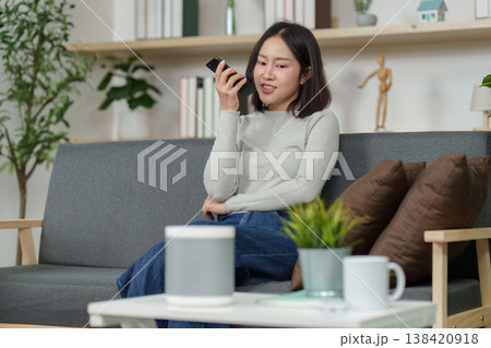 Woman speaking to smart speaker in a cozy living room Woman speaking to smart speaker in a cozy living room 138420918