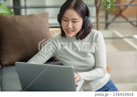 Woman using laptop with headphones in cozy home setting Woman using laptop with headphones in cozy home setting 138420928