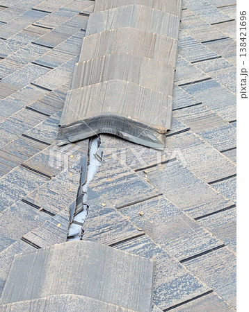 Close view of broken shingles on a roof showing cracks and wear in an urban setting during daytime 138421696