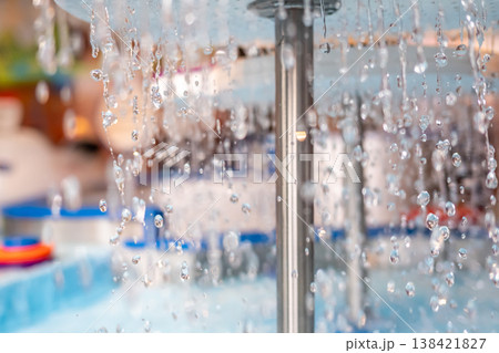 Water droplets cascade from a fountain in a vibrant outdoor setting during a sunny afternoon 138421827