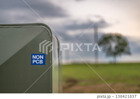 Utility box marked as non-PCB located in a green field with trees in the background during overcast weather Utility box marked as non-PCB located in a green field with trees in the background during overcast weather 138421837