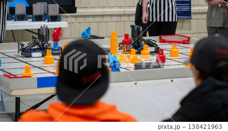 Teams compete in a robot challenge on a game table with colored blocks during a robotics event in a school gym 138421963