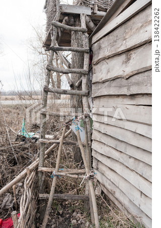 Rustic Wooden Ladder Leaning Against Weathered Barn Wall Amidst Overgrown Field With Scattered Debris And Bare Trees Under Gray Sky Rustic Wooden Ladder Leaning Against Weathered Barn Wall Amidst Overgrown Field With Scattered Debris And Bare Trees Under Gray Sky 138422262