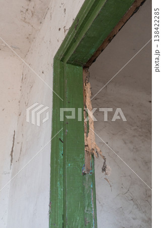 Weathered Green Wooden Door Frame With Peeling Paint Exposed Raw Wood And Cracked White Plastered Wall Background Showing Decay 138422285