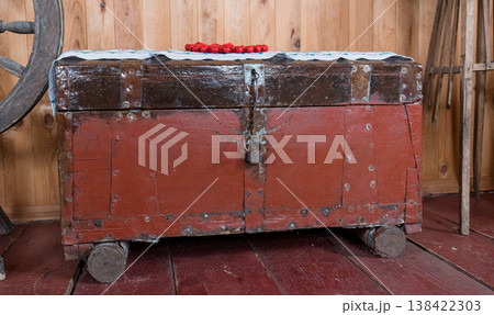 Vintage Red Wooden Trunk With Iron Rivets And Lock On Wheels Inside Rustic Barn With Wheel And Tools Background Vintage Red Wooden Trunk With Iron Rivets And Lock On Wheels Inside Rustic Barn With Wheel And Tools Background 138422303