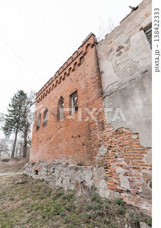 Weathered Red Brick Ruin With Gothic Arched Windows And Crumbling Stone Foundation In Overgrown Rural Landscape Under Gray Sky Weathered Red Brick Ruin With Gothic Arched Windows And Crumbling Stone Foundation In Overgrown Rural Landscape Under Gray Sky 138422333