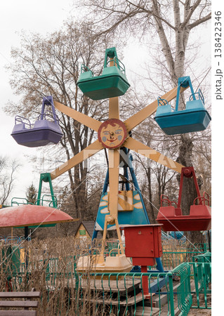 Vintage Colorful Childrens Amusement Park Ride With Swinging Seats In Overgrown Autumn Forest Setting Showing Nostalgic Mood And Faded Paint Textures 138422346