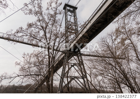Rusty Industrial Steel Trestle Bridge Tower Amidst Bare Trees Under Overcast Sky Showing Weathered Metal Structure With Crossbeams And Grating In Muted Earth Tones 138422377