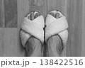 White soft slippers on women feet, top view, black and white. Homey clothing. Cozy fluffy slippers on legs, view from above, monochrome. Domestic lifestyle. Cozy clothes in spa salon. Woman after bath 138422516