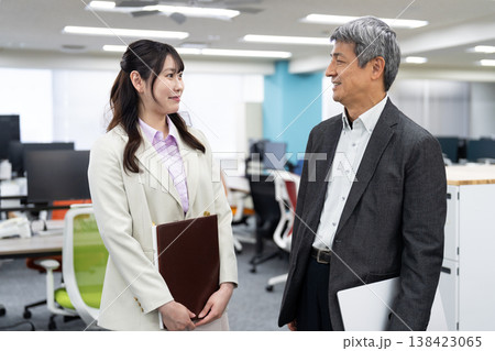 資料やパソコンを手に明るい雰囲気で立ち話をする2人の会社員 138423065