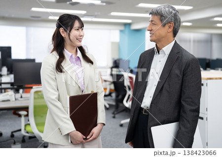 資料やパソコンを手に明るい雰囲気で立ち話をする2人の会社員 資料やパソコンを手に明るい雰囲気で立ち話をする2人の会社員 138423066