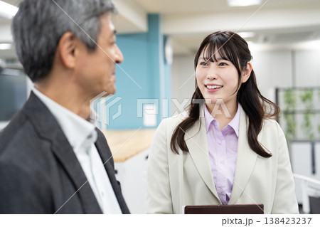資料やパソコンを手に明るい雰囲気で立ち話をする2人の会社員 資料やパソコンを手に明るい雰囲気で立ち話をする2人の会社員 138423237
