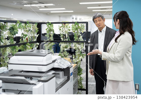 オフィスで複合機の使い方を説明する女性社員と男性上司 138423954
