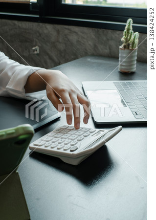 A professional working with a calculator and laptop in a modern office, highlighting productivity and technology. A professional working with a calculator and laptop in a modern office, highlighting productivity and technology. 138424252