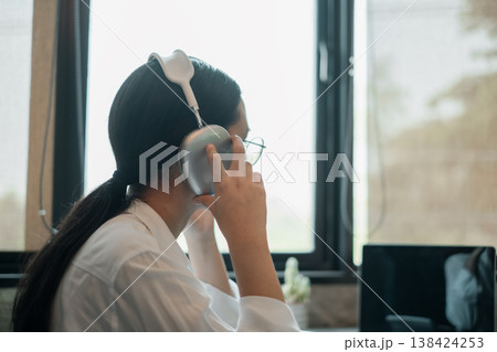 A woman wearing stylish headphones, sitting by a window, enjoying music in a bright, modern room. A woman wearing stylish headphones, sitting by a window, enjoying music in a bright, modern room. 138424253