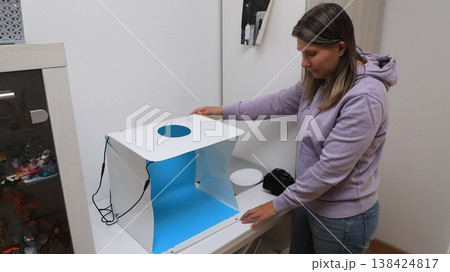 Woman sets up a lightbox for photography at home in the afternoon to take pictures of small items Woman sets up a lightbox for photography at home in the afternoon to take pictures of small items 138424817