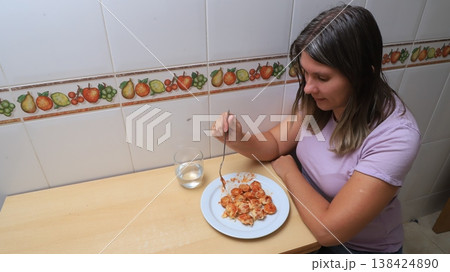 Woman seated at a wooden table enjoying a plate of pasta with tomato sauce Woman seated at a wooden table enjoying a plate of pasta with tomato sauce 138424890