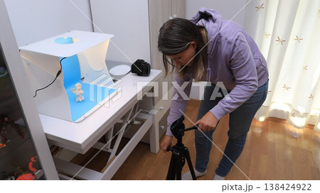 Person sets up camera equipment in a well-lit room to capture a small object  138424922