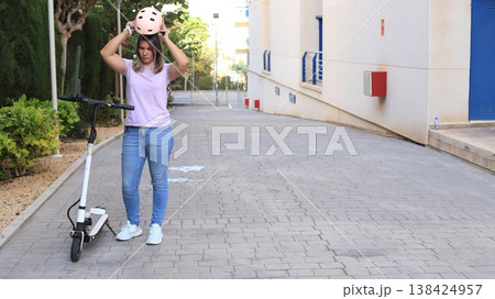Young woman wearing a helmet prepares to ride an electric scooter on a paved pathway Young woman wearing a helmet prepares to ride an electric scooter on a paved pathway 138424957