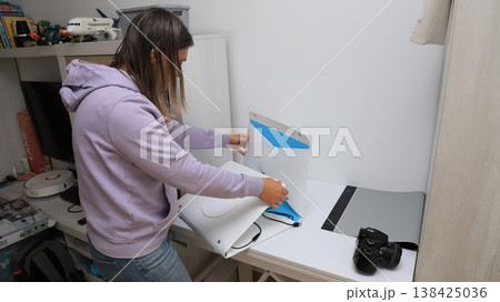 Woman sets up a device on a desk in a home office space while organizing equipment  138425036