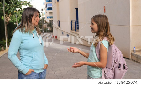 Caring mother in light blue hoodie listens attentively to her smiling daughter 138425074