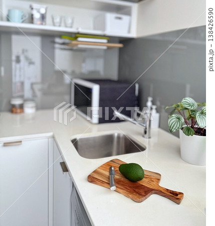 清潔感のある白いキッチンのカウンターにアボカドとナイフを置いた木製まな板 138426590