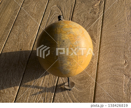 Vintage-style globe standing on a textured wooden surface in warm natural light. Visible map details Vintage-style globe standing on a textured wooden surface in warm natural light. Visible map details 138426819