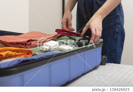 Travel camera and electronic gear lie beside an open suitcase during indoor packing. Cropped female Travel camera and electronic gear lie beside an open suitcase during indoor packing. Cropped female 138426925