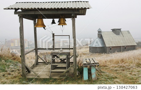 Rustic wooden bell tower with hanging brass bells stands on a frosty hillside. Rustic wooden bell tower with hanging brass bells stands on a frosty hillside. 138427063