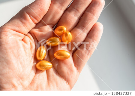 Hand holding shiny golden softgel capsules, representing supplements, vitamins, and medication for health, beauty, and wellness. Healthy lifestyle, self-care 138427327