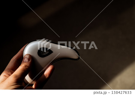 Hand holding modern microcurrent facial massager in warm sunlight with deep shadows, aesthetic beauty tech, minimalist skin care routine at home, sculptural guasha device, moody wellness concept. Hand holding modern microcurrent facial massager in warm sunlight with deep shadows, aesthetic beauty tech, minimalist skin care routine at home, sculptural guasha device, moody wellness concept. 138427633