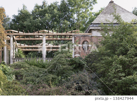 An elegant wooden pergola supported by stone columns stands nestled among lush, overgrown greenery, adjacent to a classic brick garden structure with a prominent shingled roof at The Hill Garden and An elegant wooden pergola supported by stone columns stands nestled among lush, overgrown greenery, adjacent to a classic brick garden structure with a prominent shingled roof at The Hill Garden and 138427944