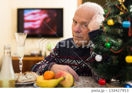 Lonely frustrated gray-haired senior man sitting at home table during Christmas celebration Lonely frustrated gray-haired senior man sitting at home table during Christmas celebration 138427953