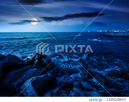 sea coast with stones and boulders at night. view of beach with rock in seaweed. full moon over dynamic cloudscape on the sky above horizon. mysterious summer vacations background concept 138429603