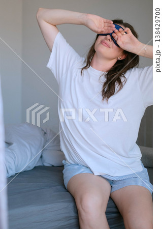Woman wakes in soft pajamas after sleep on orthopedic pillow and mattress with sleep mask showing importance of quality sleep for health Woman wakes in soft pajamas after sleep on orthopedic pillow and mattress with sleep mask showing importance of quality sleep for health 138429700