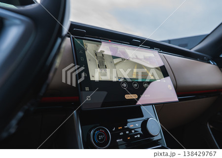 Close up interior shows a large touchscreen with 360 parking camera and rear guidelines, tan dashboard and red trim, soft light, shallow depth, workshop inspection focus. 138429767
