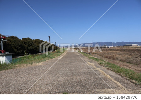 青空と川の堤防のまっすぐの道と遠くに見える山と街の風景 青空と川の堤防のまっすぐの道と遠くに見える山と街の風景 138429770