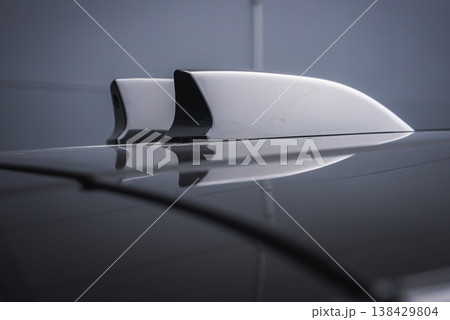 Close up of white shark fin roof antenna and smaller fin on glossy roof, mirrored on surface in an indoor workshop with cool lighting, emphasizing high end design. Close up of white shark fin roof antenna and smaller fin on glossy roof, mirrored on surface in an indoor workshop with cool lighting, emphasizing high end design. 138429804