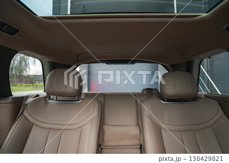 Tan leather rear seats with sculpted headrests face the back window and sunroof. Soft lighting reveals stitching, chrome details, and a modern facility outside. Tan leather rear seats with sculpted headrests face the back window and sunroof. Soft lighting reveals stitching, chrome details, and a modern facility outside. 138429821